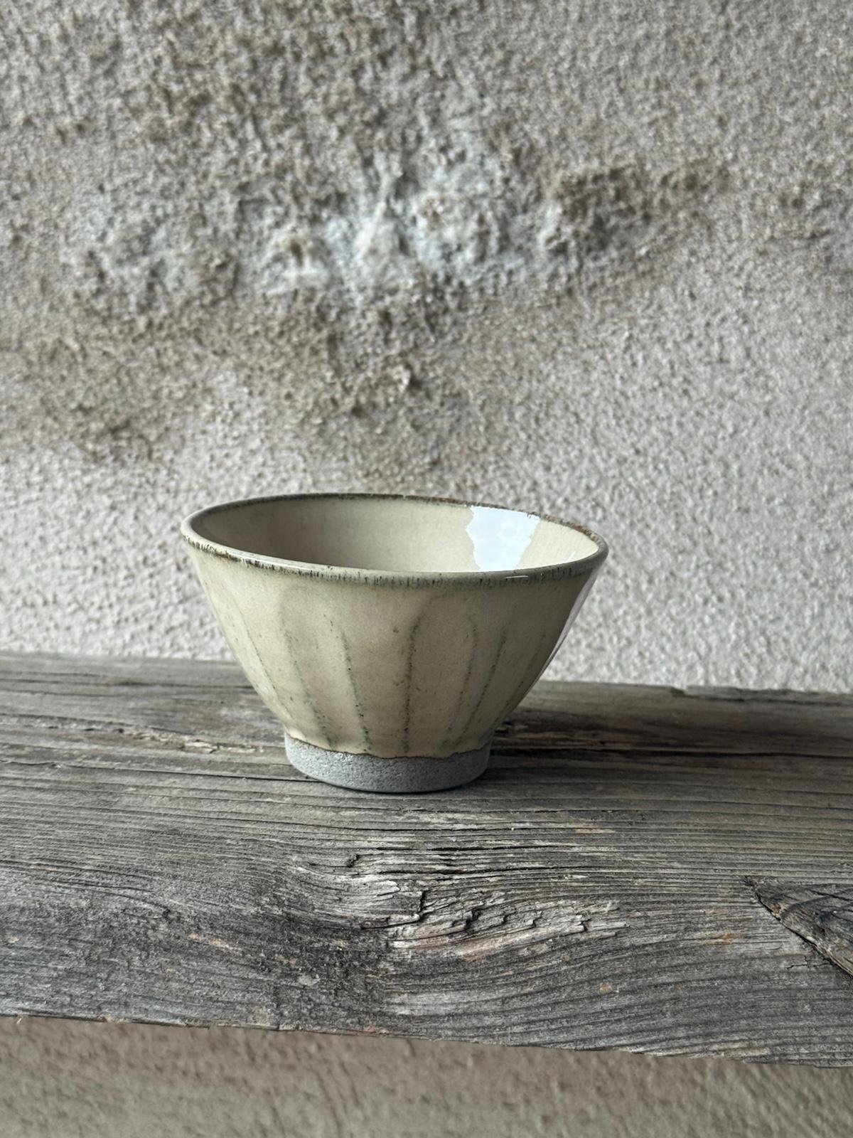 Kom in beige glazuur met fijne ingekerfde lijnen, van voren gezien op een houten plank
