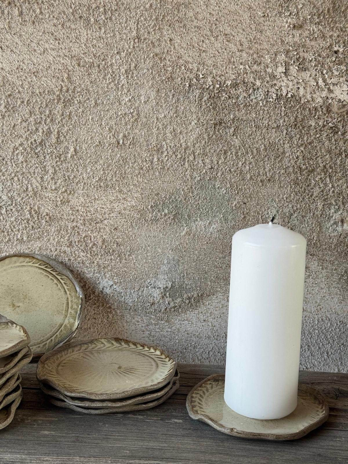 Stapels kleine bordjes met ingekerfd bladmotief, met een witte stompkaars op een bordje ernaast