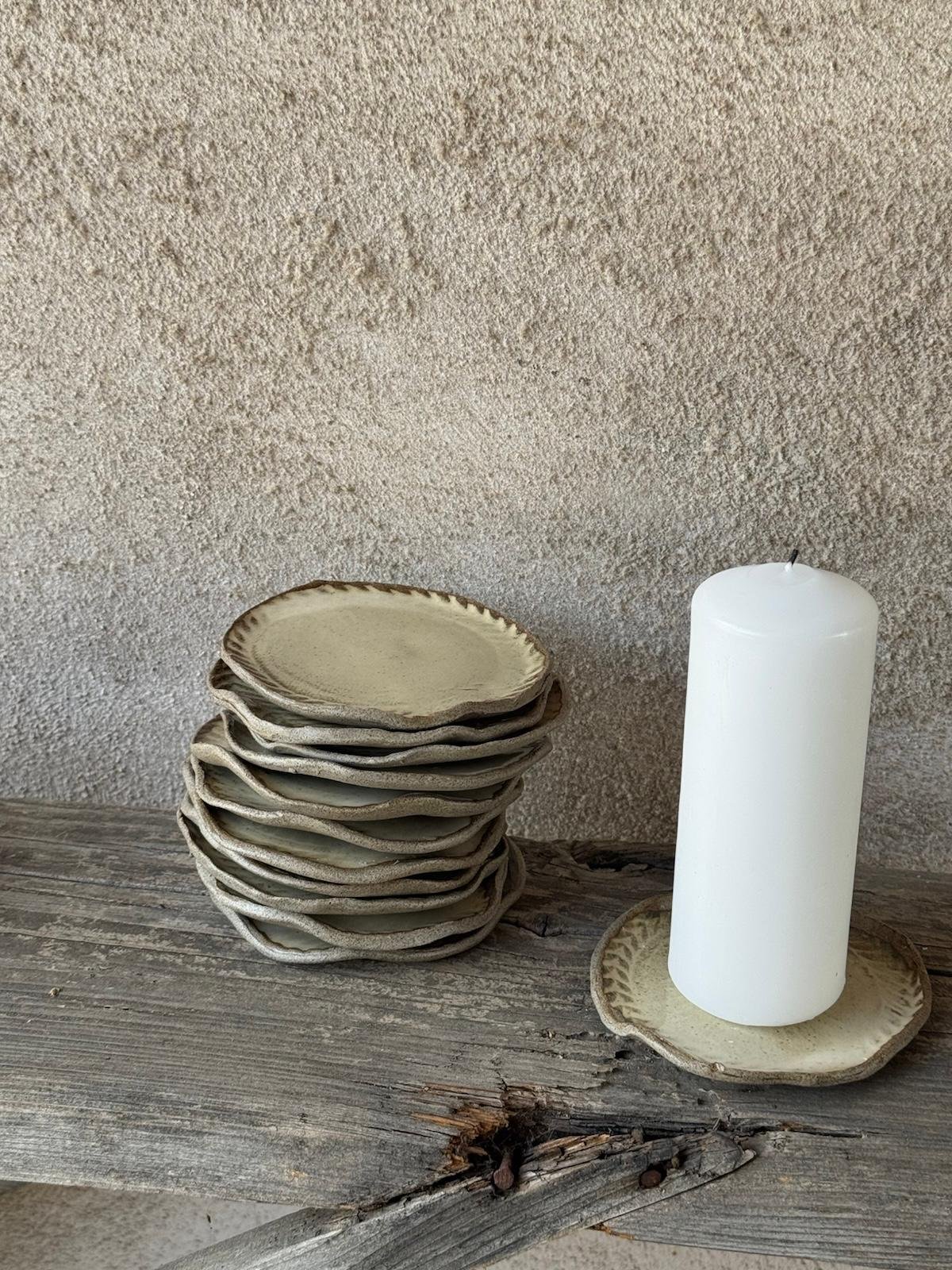 Stapel van tien kleine beige bordjes naast een witte stompkaars op een bordje