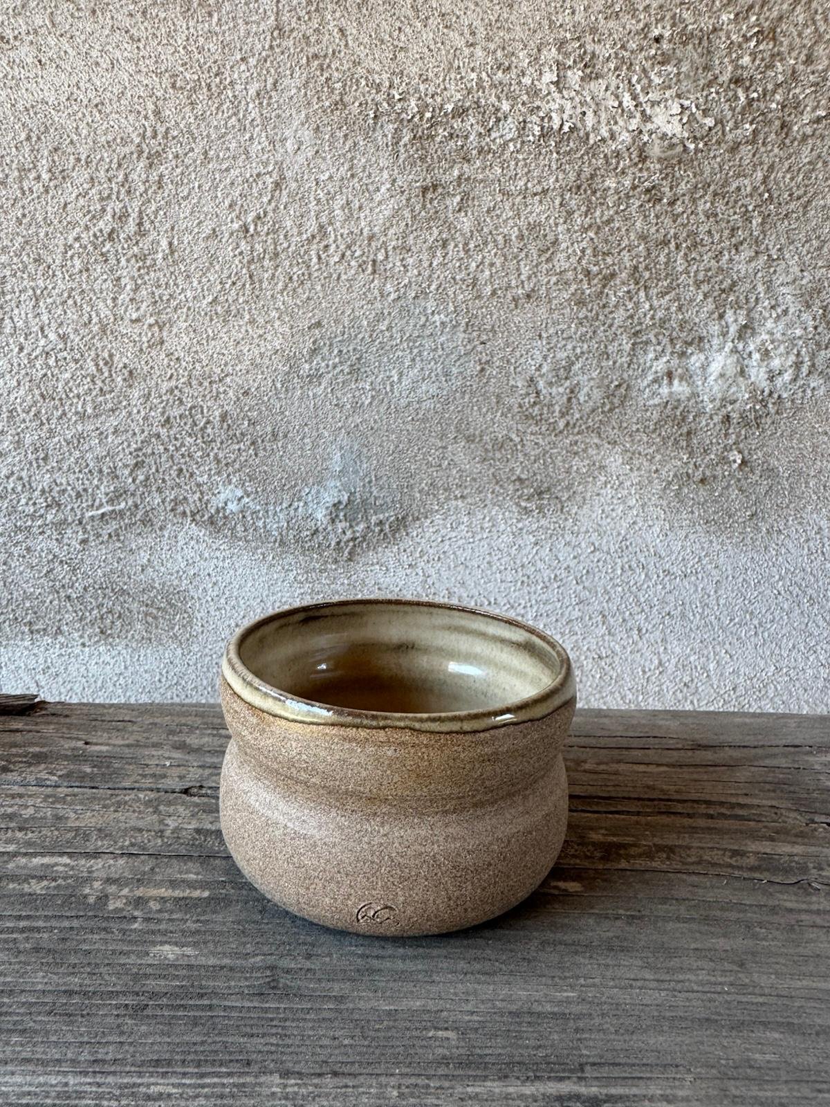 Twee beige bekers met zachte glazuurtinten naast elkaar op een houten plank