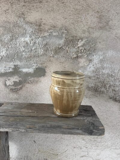 Gedraaide vaas in warme okertinten met zichtbare draailijnen, op een houten plank