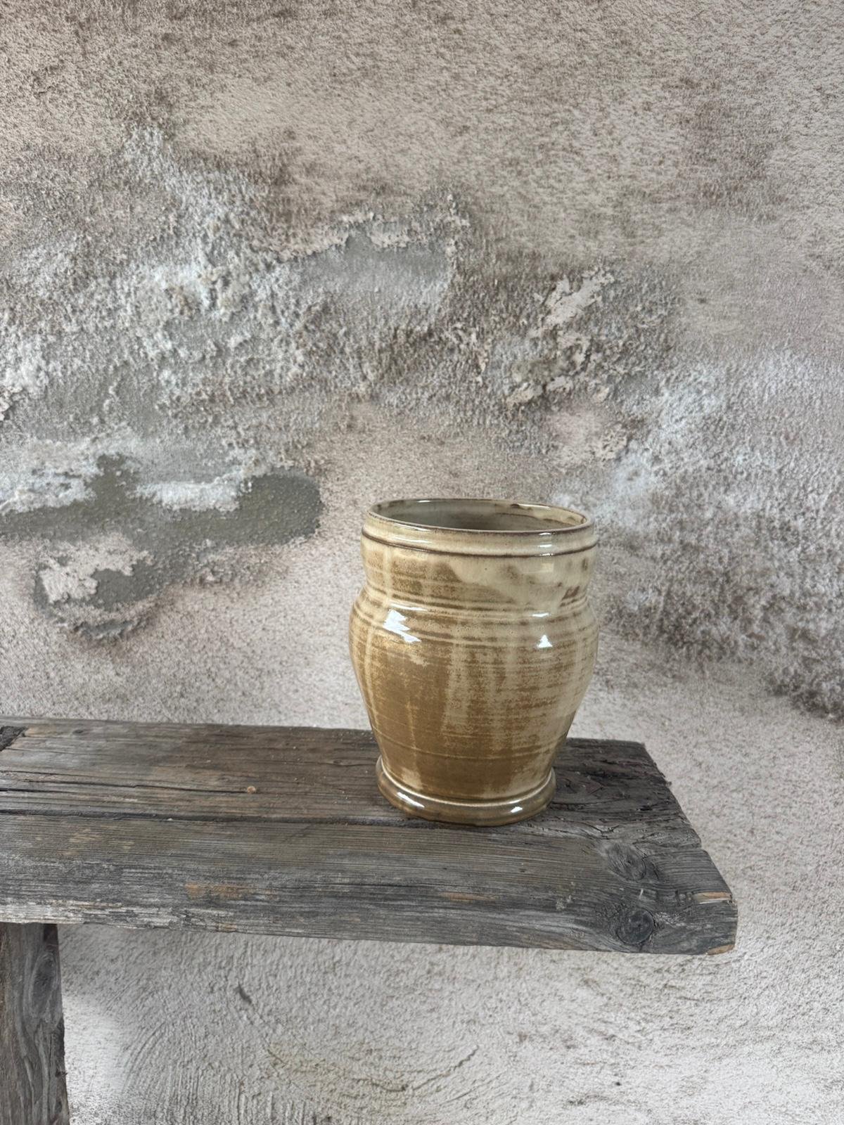 Gedraaide vaas in warme okertinten met zichtbare draailijnen, op een houten plank