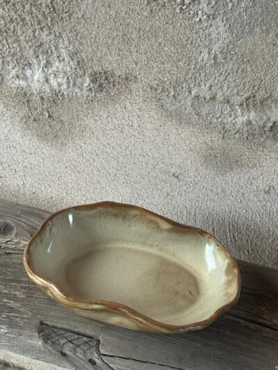 Ovale serveerschaal in okergeel glazuur met een golvende rand, op een houten plank