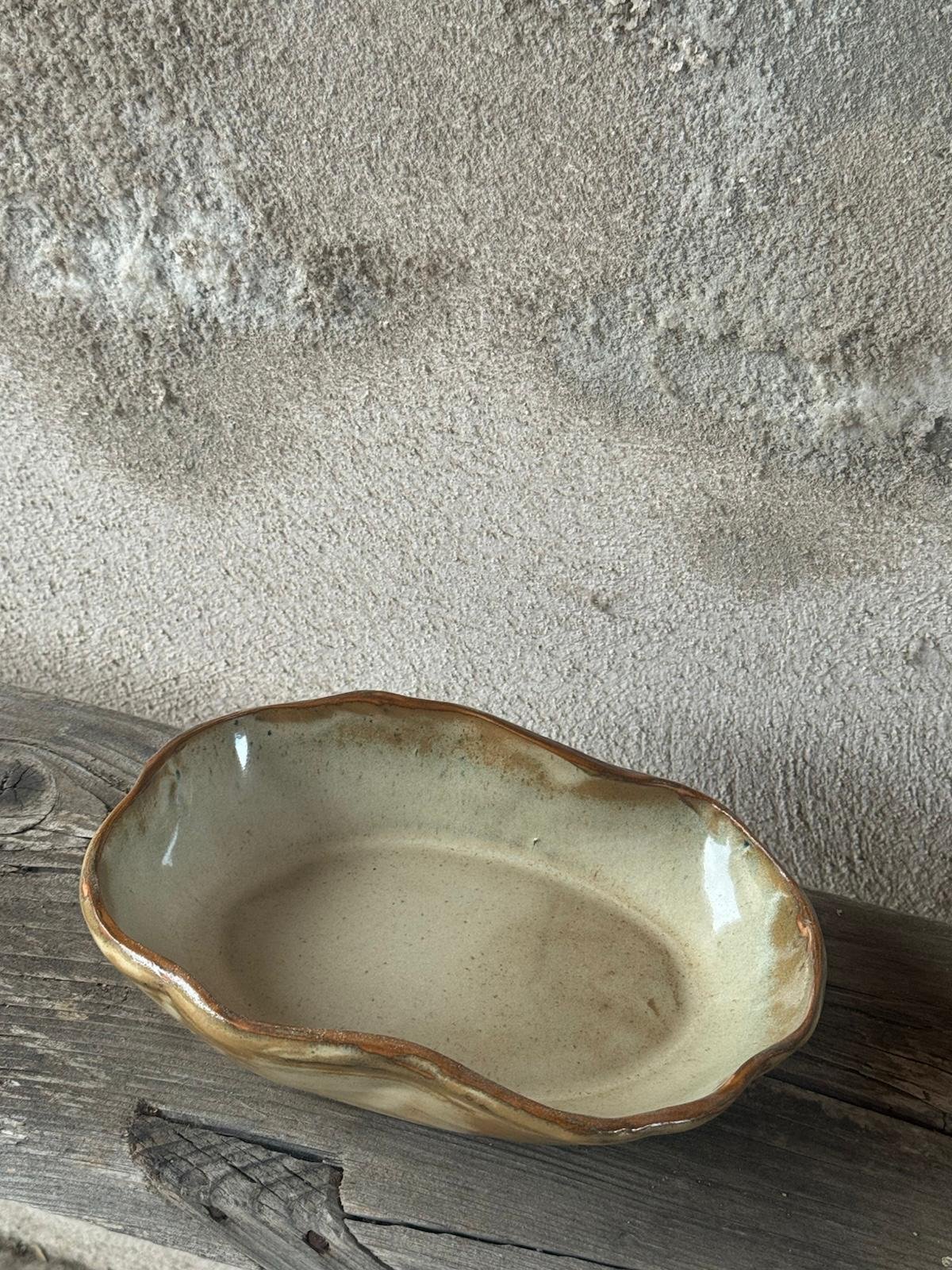 Ovale serveerschaal in okergeel glazuur met een golvende rand, op een houten plank