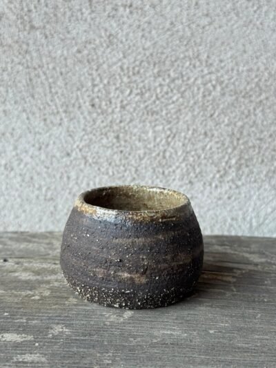 Kleine handgemaakte espressokop uit donkere, ruwe klei op een verweerde houten plank
