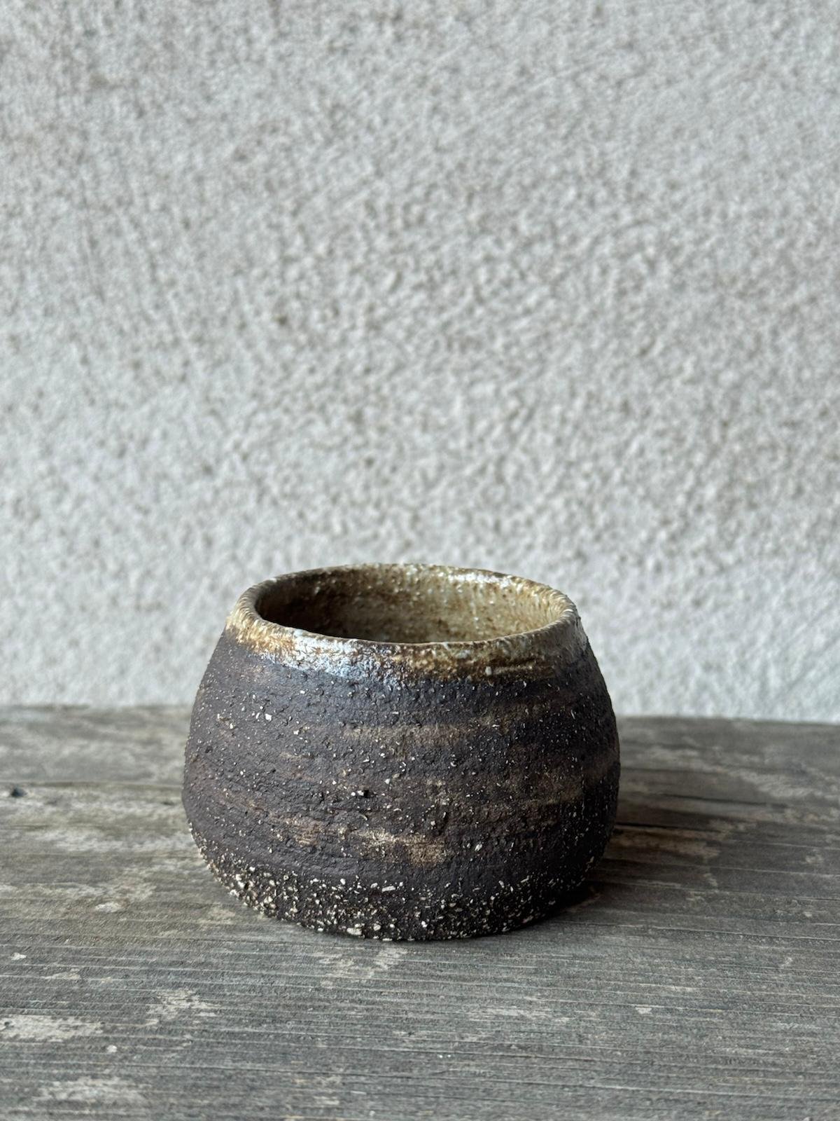 Kleine handgemaakte espressokop uit donkere, ruwe klei op een verweerde houten plank