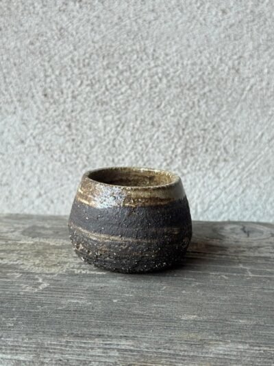 Kleine handgemaakte espressokop uit donkere klei met een lichte, onregelmatige rand