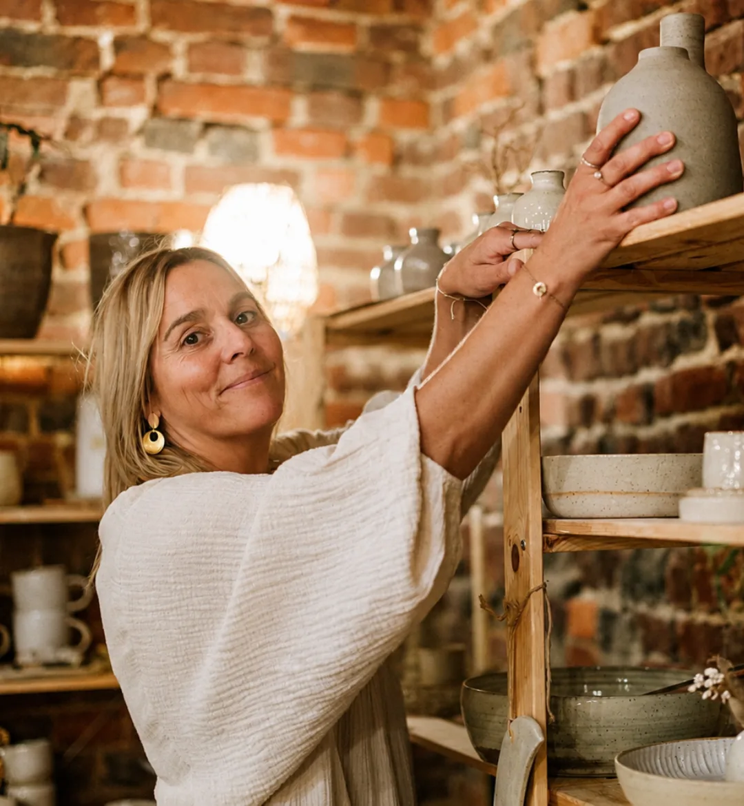 Vanessa Schaeken zet een keramieken vaas op een houten rek in haar atelier