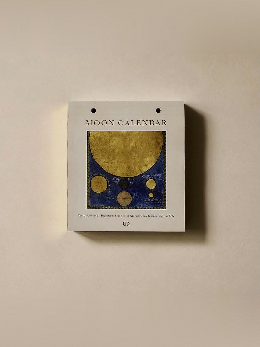 Voorkant van de Moon Calendar 2027 van Moonsisters: een gouden maan met planeten op een blauwe illustratie