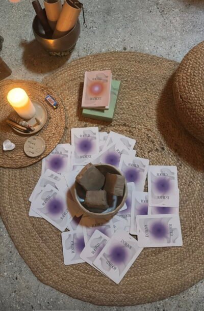 Kaarten met de tekst ROOTED RADIANT rond een schaal met stukken klei, naast een brandende kaars.